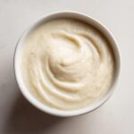 Overhead view of a bowl filled with smooth, creamy roasted cauliflower soup, showing swirl marks from serving.