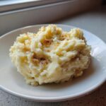 A scoop of creamy roasted garlic mashed potatoes topped with browned garlic pieces on a white plate.