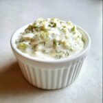 Close-up of creamy homemade tartar sauce recipe, featuring chopped pickles and fresh dill, served in a small white ramekin.