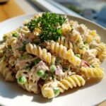 Close-up of creamy tuna pasta salad made with rotini pasta, green peas, red onion, and topped with fresh parsley.