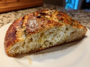 Close-up of a thick slice of crusty bread showing an open, airy crumb texture and rosemary topping.