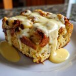 A square serving of baked eggs benedict casserole topped with melted cheese or hollandaise sauce.