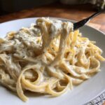 Close-up of fettuccine noodles coated in creamy vegan alfredo sauce being lifted by a fork.