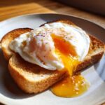 Close-up of a perfectly poached egg with a runny yolk spilling onto two slices of golden toast.