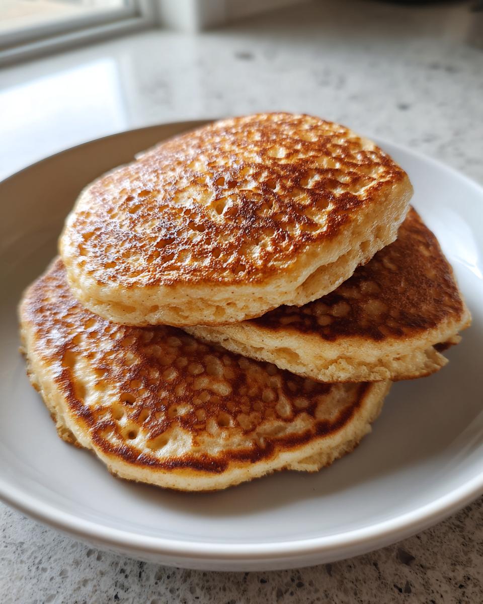 A stack of three golden-brown, fluffy coconut flour pancakes served on a white plate.