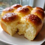 Close-up of fluffy, pull-apart dinner rolls with a shiny, golden-brown glaze, one roll having a piece torn away.