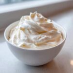 Close-up of creamy, fluffy homemade fruit dip filling a small white bowl.