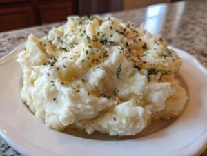 A generous serving of creamy roasted garlic mashed potatoes topped with melted butter and fresh thyme.
