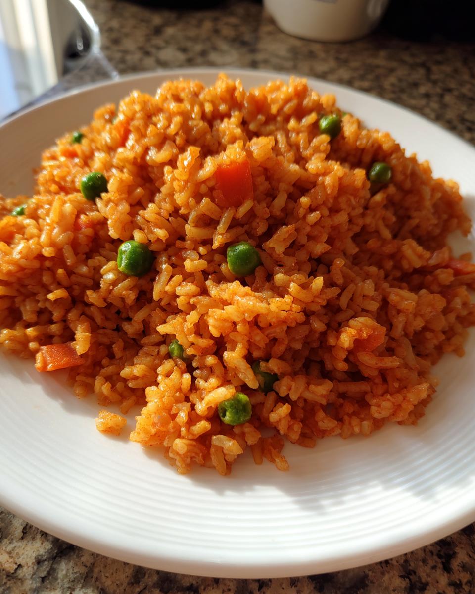 A close-up of fluffy, orange-red Spanish rice mixed with bright green peas and diced carrots served on a white plate.