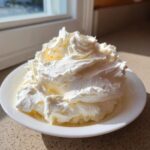 A generous swirl of fluffy, white vanilla buttercream frosting piled high on a small white plate.