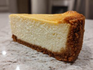 A thick, creamy slice of new york cheesecake with a golden top and graham cracker crust.