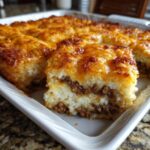 Close-up of a square serving of tater tot casserole showing layers of ground beef and creamy potato topping with melted cheese.