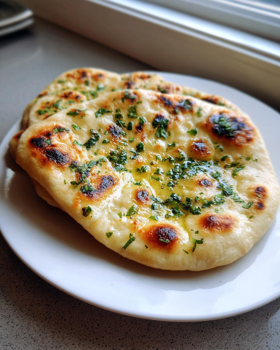 Two pieces of freshly baked naan bread brushed with melted butter and topped with chopped cilantro, resting on a white plate.