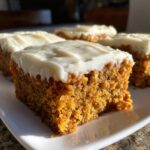 A close-up of a moist square of carrot cake bars topped with thick cream cheese frosting.