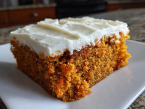 A square slice of moist carrot cake bars topped with thick, creamy white frosting, served on a white plate.