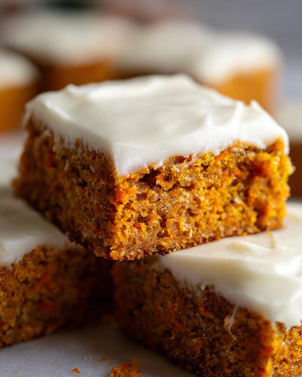 A close-up stack of moist, orange carrot cake bars topped with thick white cream cheese frosting.
