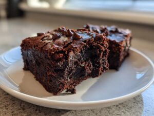 Two rich, fudgy date brownies topped with chocolate chips sitting on a white plate.