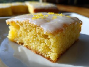 A close-up of a single square of fudgy lemon brownies topped with white glaze and lemon zest.