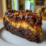 A decadent slice of german chocolate cheesecake showing a dark brownie base, creamy layer, and gooey coconut-pecan topping.