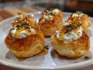 Close-up of flaky pastry puff topped with creamy goat cheese and drizzled with honey, garnished with thyme for perfect goat cheese and honey bites.