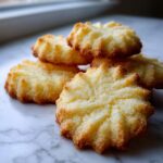 A stack of golden brown, star-shaped 3-ingredient butter cookies resting on a white marble surface.