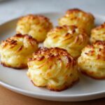 Close-up of perfectly piped and baked duchess potatoes with golden, crispy edges on a white serving plate.