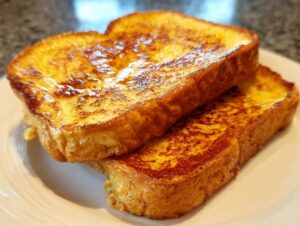 Close-up of two golden brown slices of perfectly cooked french toast stacked on a white plate.