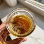 Overhead view of freshly mixed golden salad dressing with small bubbles in a clear glass jar.