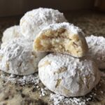 A stack of incredibly soft, gooey butter cookies generously coated in white powdered sugar, one cookie is broken open.