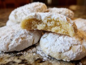 A stack of rich, tender gooey butter cookies generously dusted with powdered sugar, one cookie broken open.