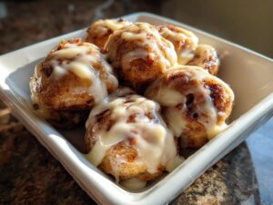 A close-up of several gooey cinnamon roll bites topped with thick white icing in a small white dish.