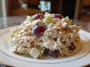 A mound of creamy greek yogurt chicken salad mixed with celery and red grapes served on a white plate.