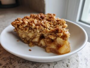 A close-up of a warm slice of apple crisp showing tender, spiced apples beneath a thick, golden oat crumble topping.