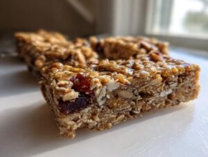 Close-up cross-section of a chewy homemade granola bar showing oats, nuts, seeds, and dried cranberries.