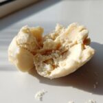 Close-up of creamy, slightly crumbly homemade marzipan recipe dough broken in half on a white surface.