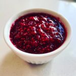 A close-up shot of thick, vibrant red homemade raspberry jam filling a small white ramekin.