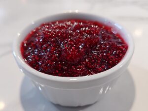 A close-up view of thick, vibrant red homemade raspberry jam filling a small white ramekin.