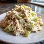 A mound of creamy honey mustard chicken salad featuring shredded chicken and chopped celery on a white plate.