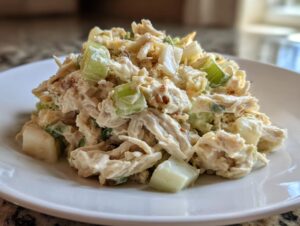 Close-up of a mound of creamy honey mustard chicken salad with visible chunks of celery on a white plate.