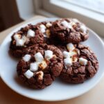 A plate of rich, dark chocolate hot chocolate cookies topped with melted white marshmallows.