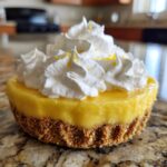 Close-up of a single-serving lemon pie with a graham cracker crust, bright yellow filling, and generous whipped cream topping.