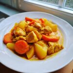 Close-up of Jamaican curry chicken served with chunks of potato and bright orange carrots in a rich yellow sauce.