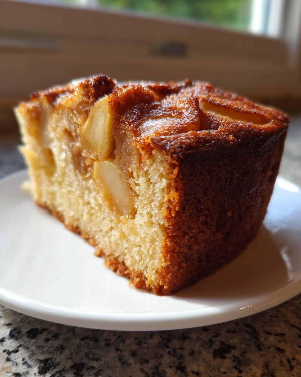 A close-up of a moist slice of jewish apple cake with visible apple pieces baked into the top.