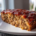 Close-up of a thick slice of juicy meatloaf topped with a shiny, dark red glaze.