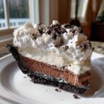 A decadent slice of layered oreo pie showing a dark crust, chocolate mousse, white filling, and whipped cream topping.