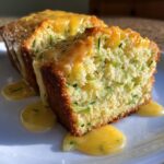 Close-up of two slices of moist lemon zucchini bread topped with a bright yellow lemon glaze.