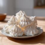 A close-up of several light, white, piped meringue cookies piled high on a small plate.