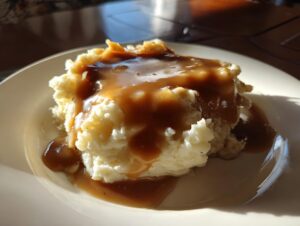 A scoop of fluffy mashed potatoes generously topped with rich, brown chicken gravy on a white plate.