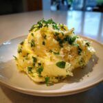 A scoop of creamy mashed potatoes generously topped with melted garlic butter and fresh chopped parsley.