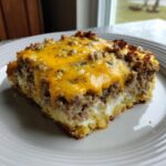 A square serving of meatloaf casserole topped with melted cheddar cheese, resting on a white plate.